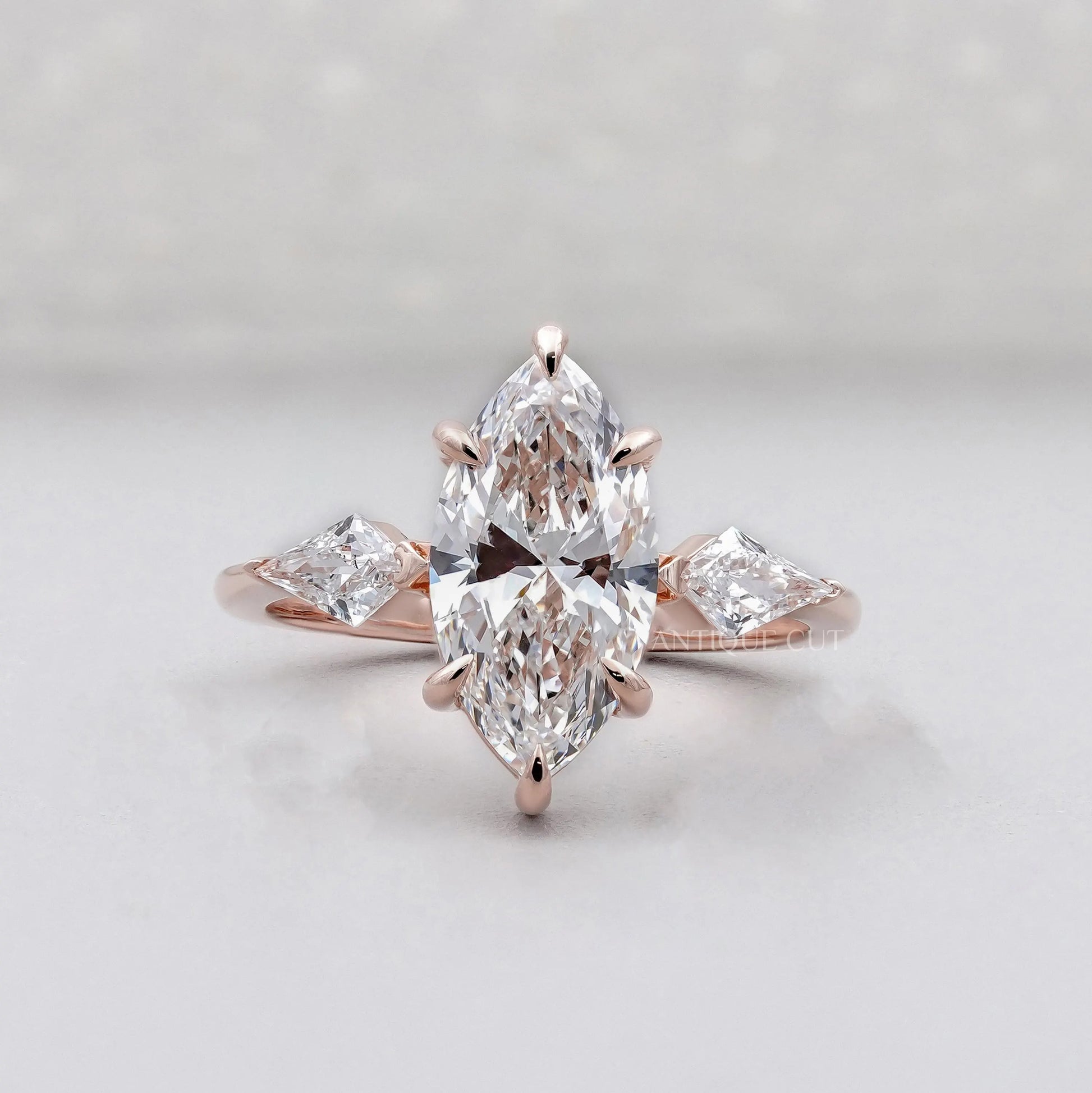 Rose gold ring with pear-shaped diamonds on a light gray background

