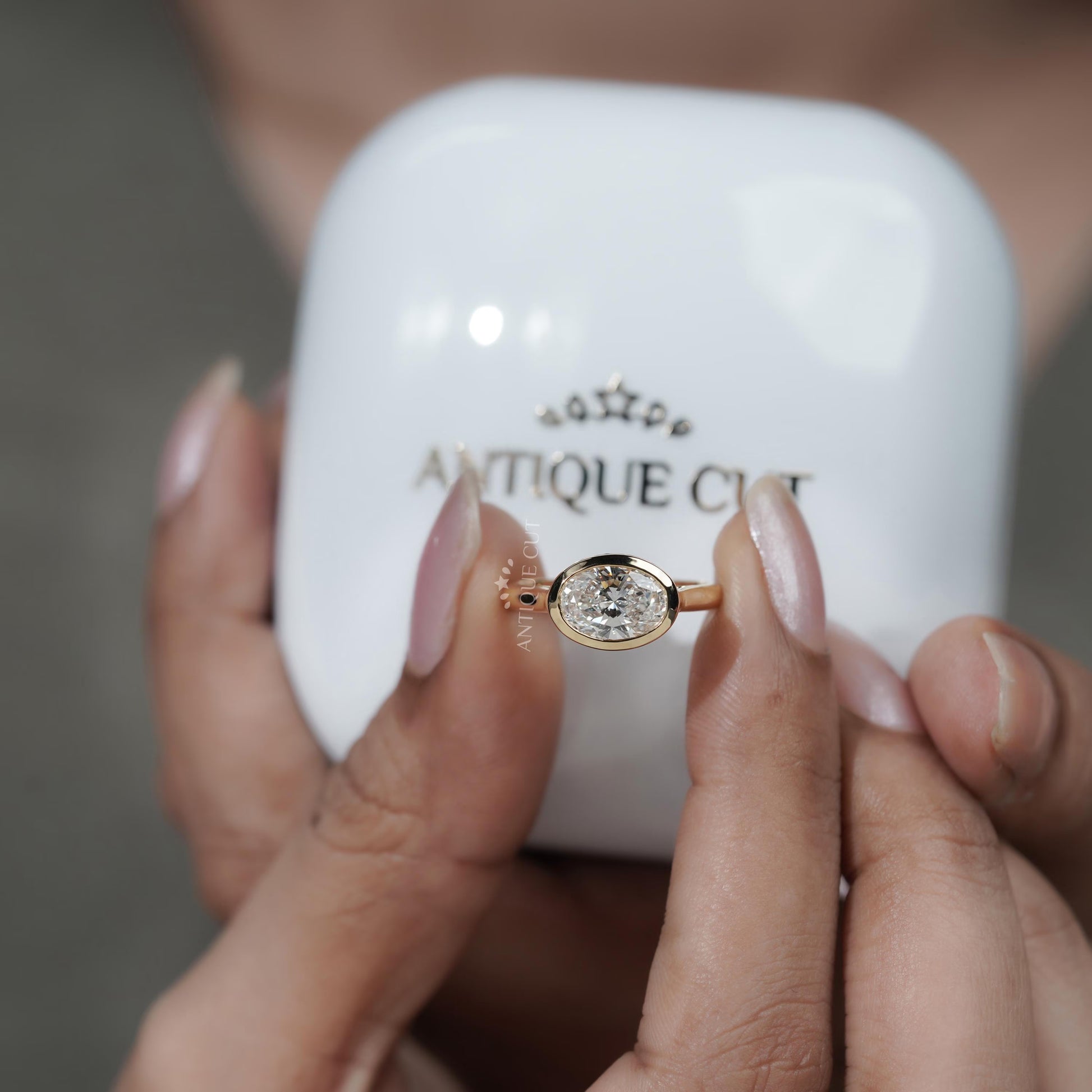 Gold ring with a diamond held by hands in front of an 'Antiquecut' jewelry box.

