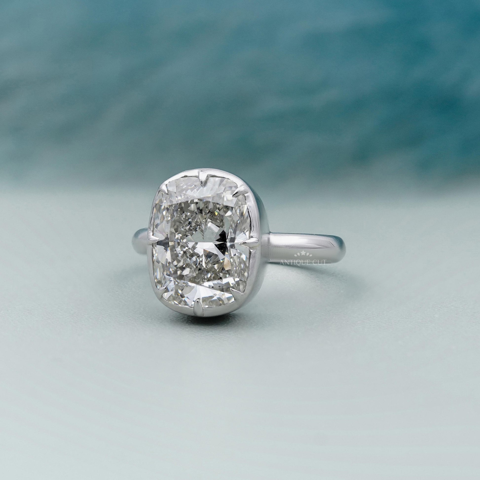 Diamond ring with a cushion-cut diamond on a light gray background

