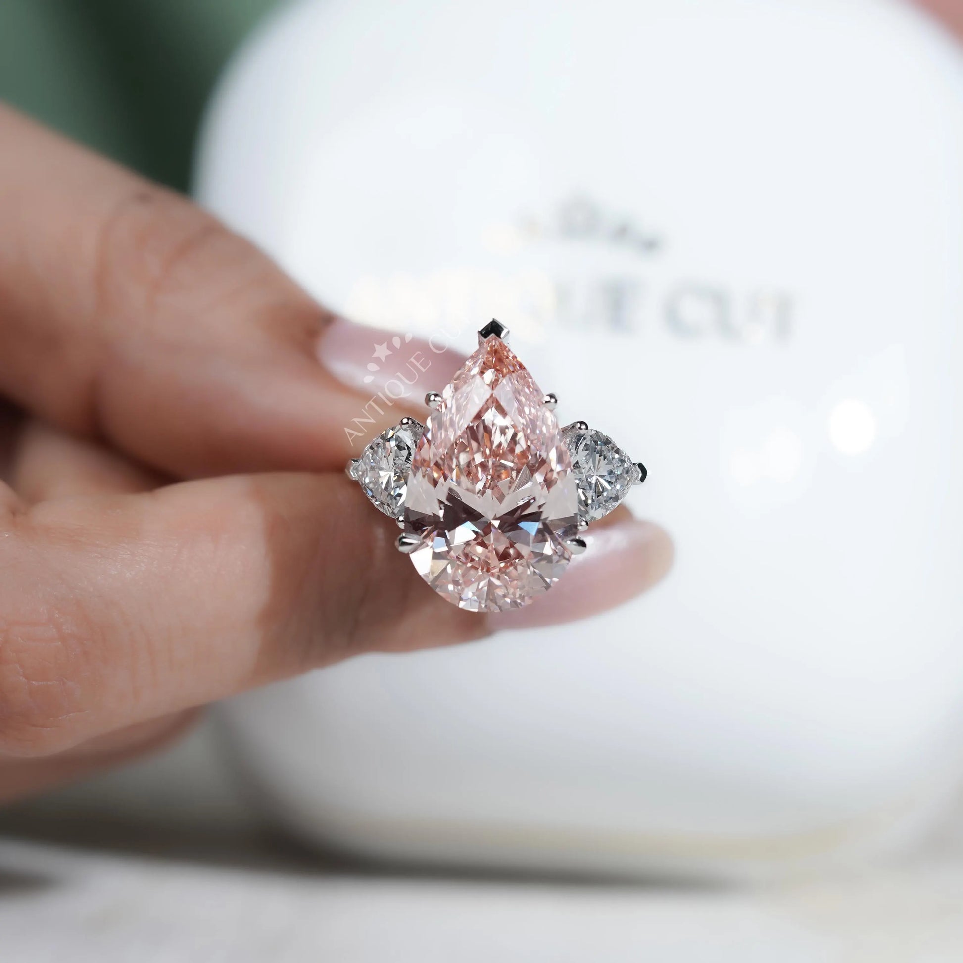 Pink diamond ring held by a hand with a blurred background


