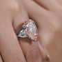 Pink pear-shaped diamond ring on a finger with a blurred background

