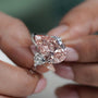 Close-up of a pink diamond ring held between fingers with a blurred background

