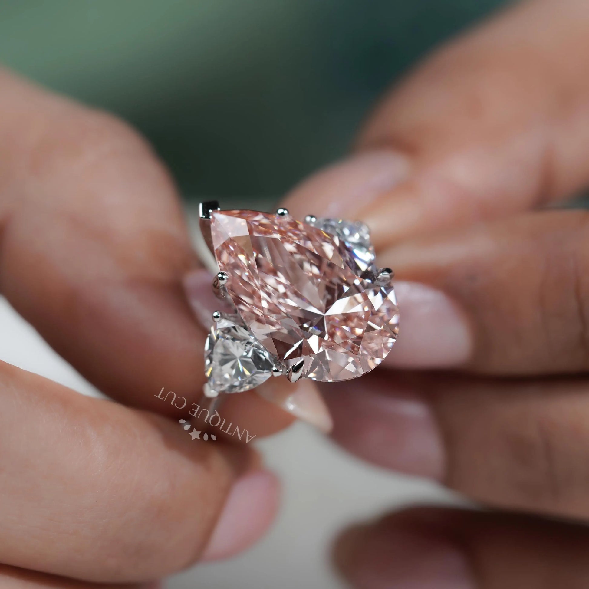 Close-up of a pink diamond ring held between fingers with a blurred background

