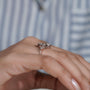 Rose gold ring with diamonds on a person's finger against a blurred striped background

