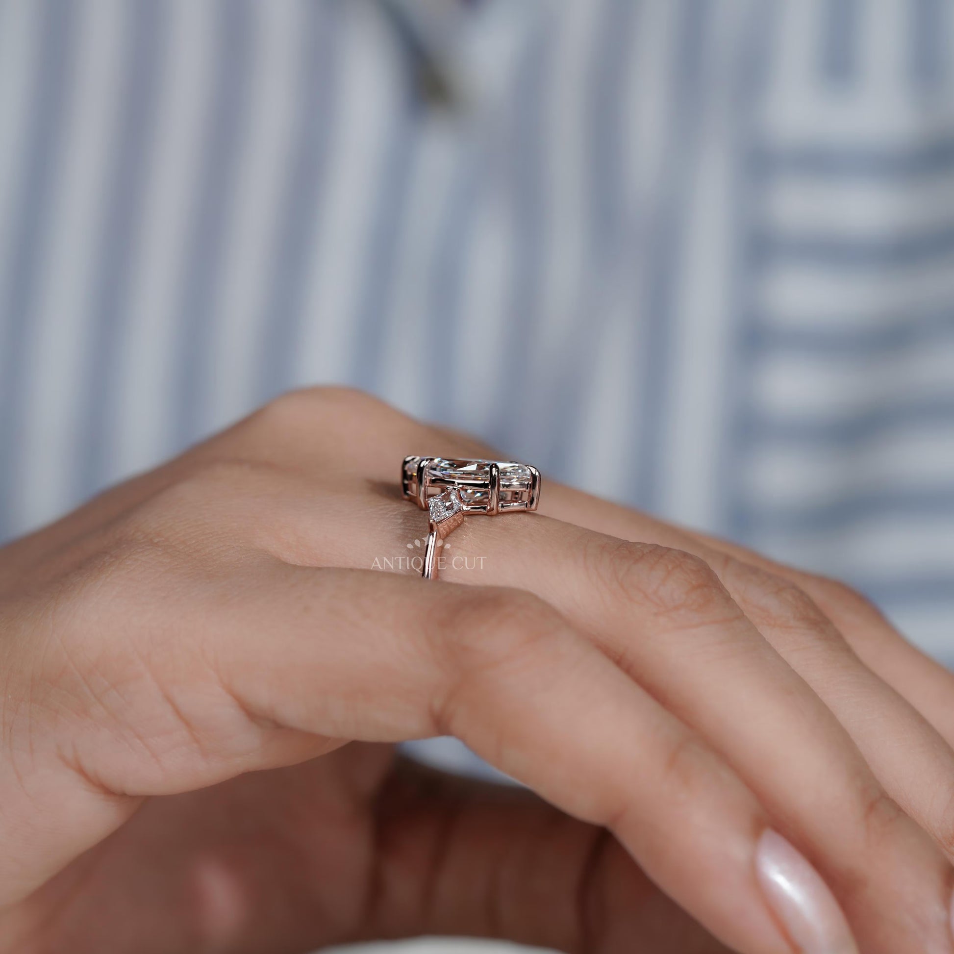 Rose gold ring with diamonds on a person's finger against a blurred striped background

