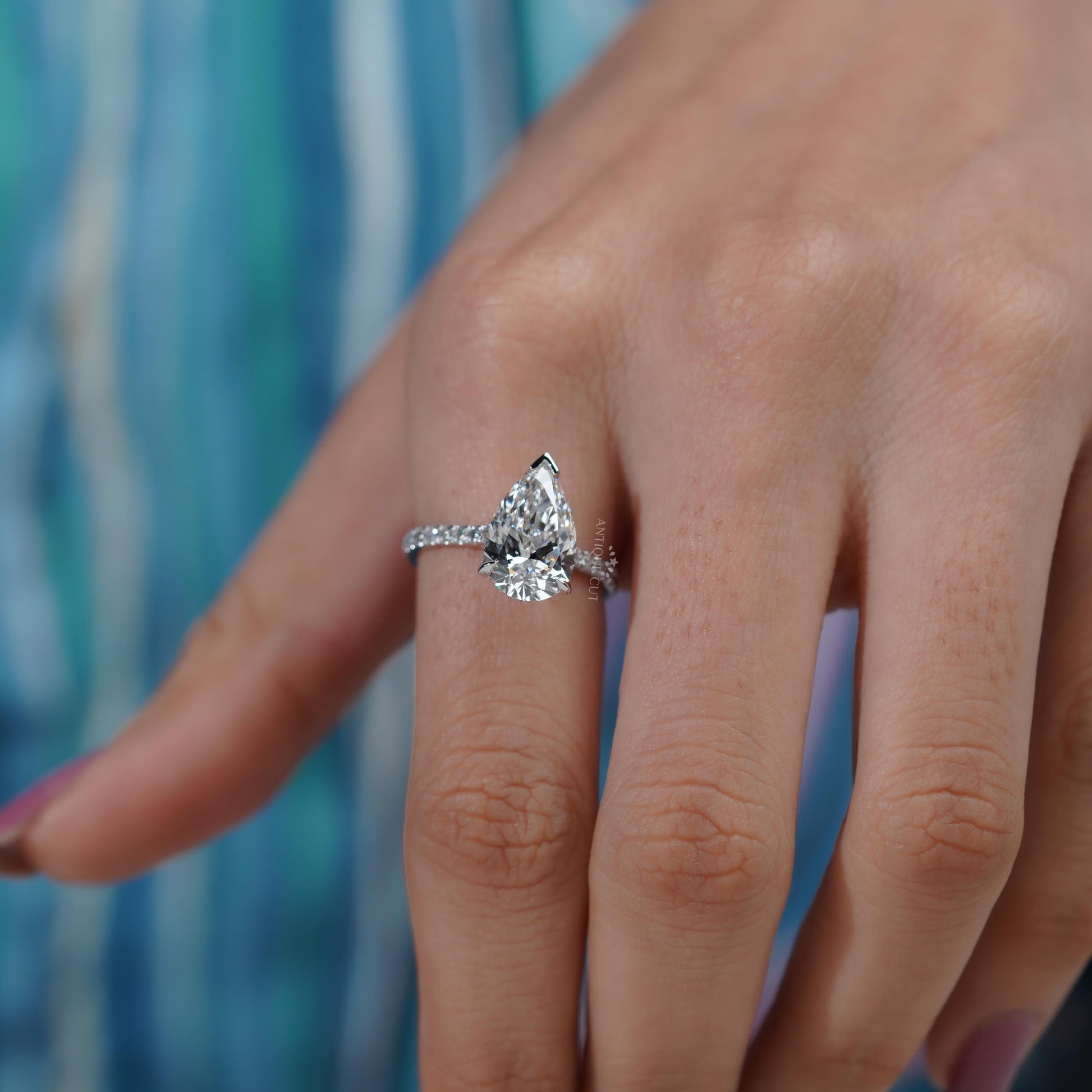 Diamond ring with a pear-shaped center stone on a soft blue background

