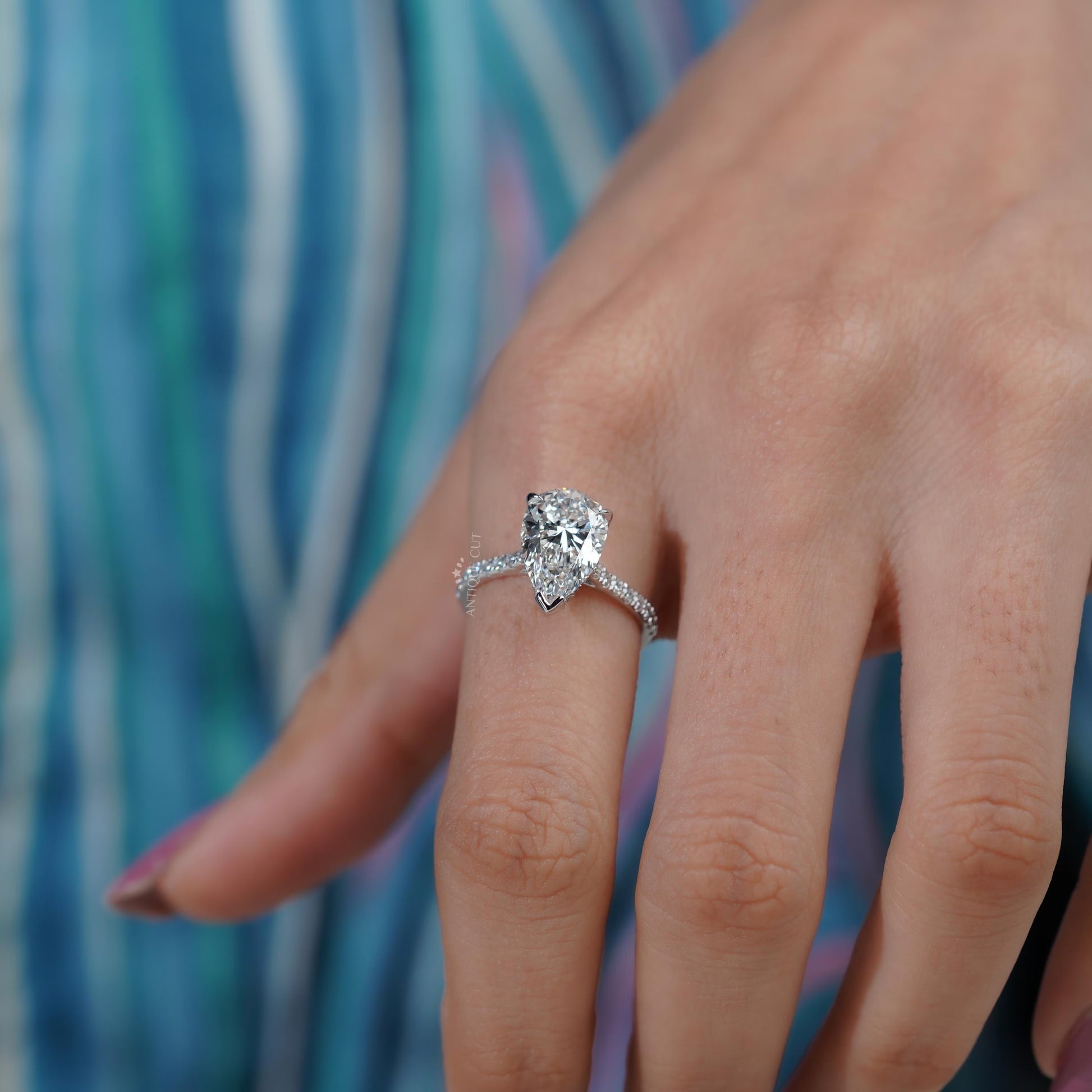 Diamond ring with a pear-shaped center stone on a soft blue background

