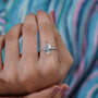 Diamond ring with a pear-shaped center stone on a soft blue background


