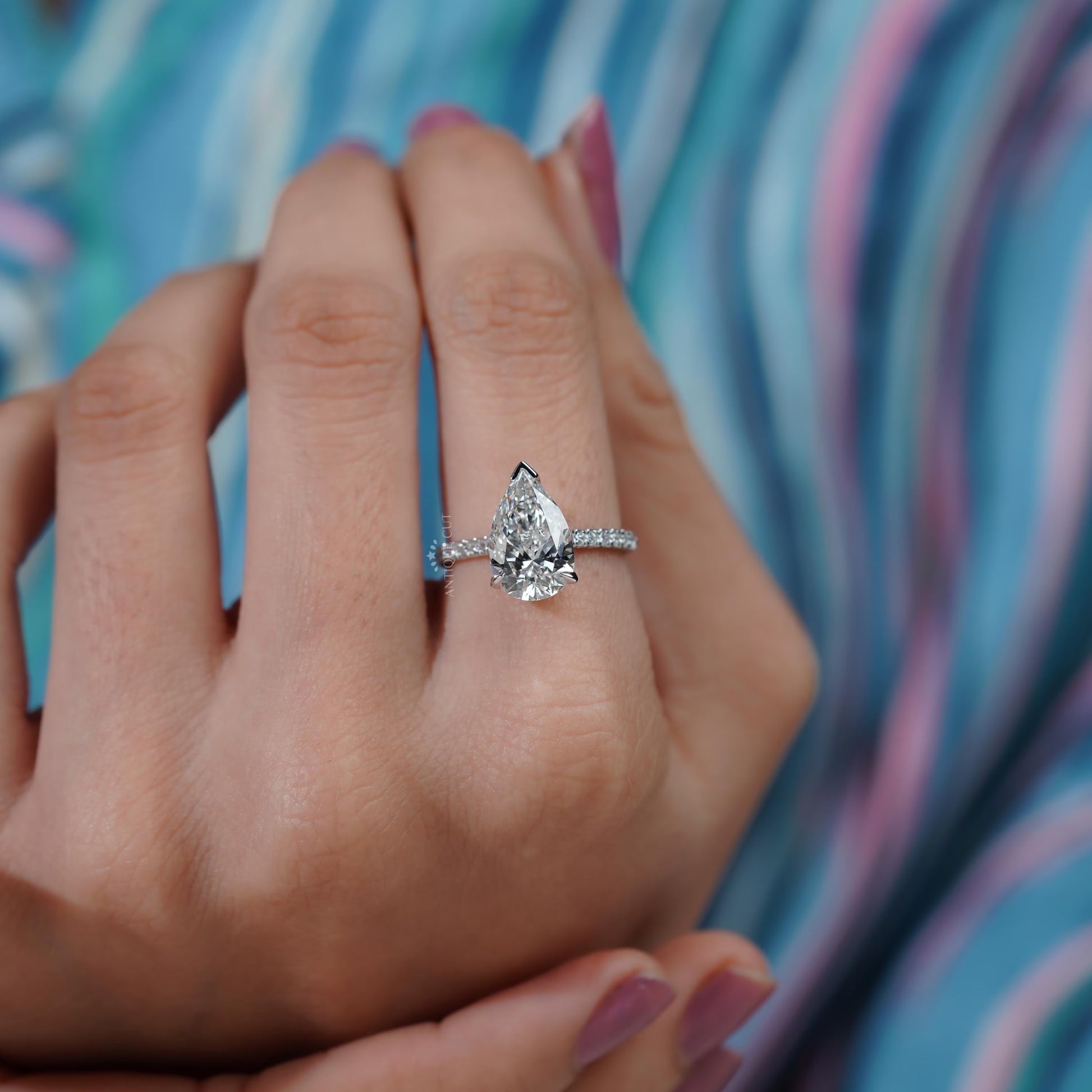 Diamond ring with a pear-shaped center stone on a soft blue background

