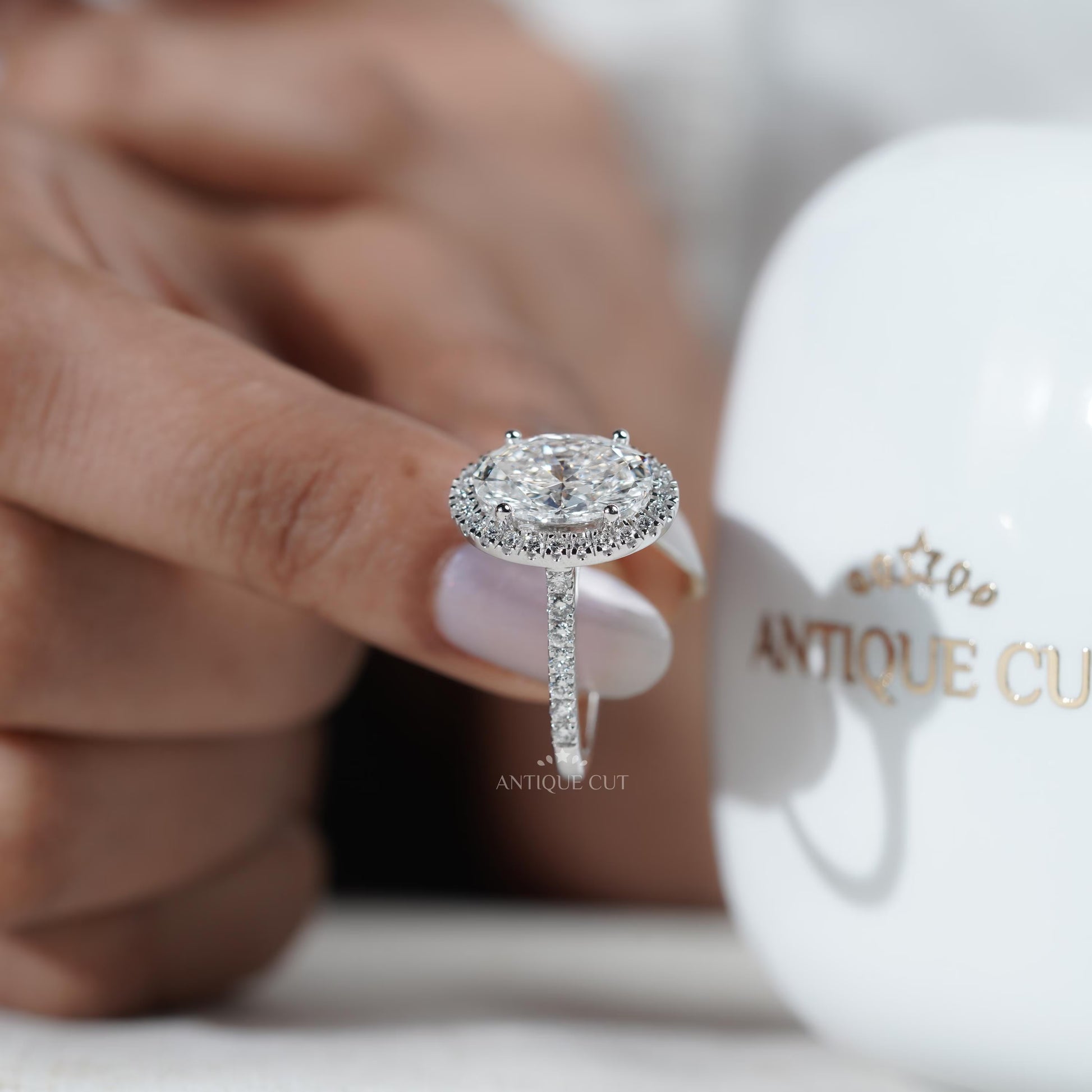 Diamond ring held by a hand with 'AntiqueCut' branding in the background

