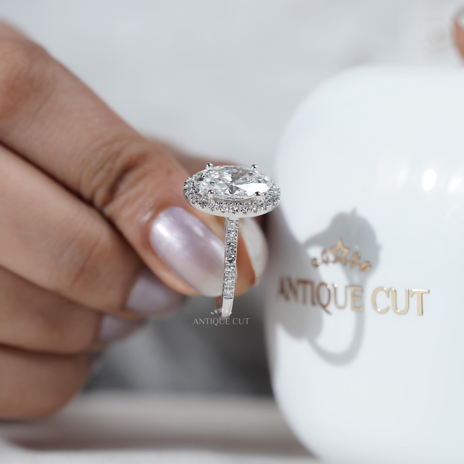 Diamond ring held by a hand with 'AntiqueCut' branding in the background
