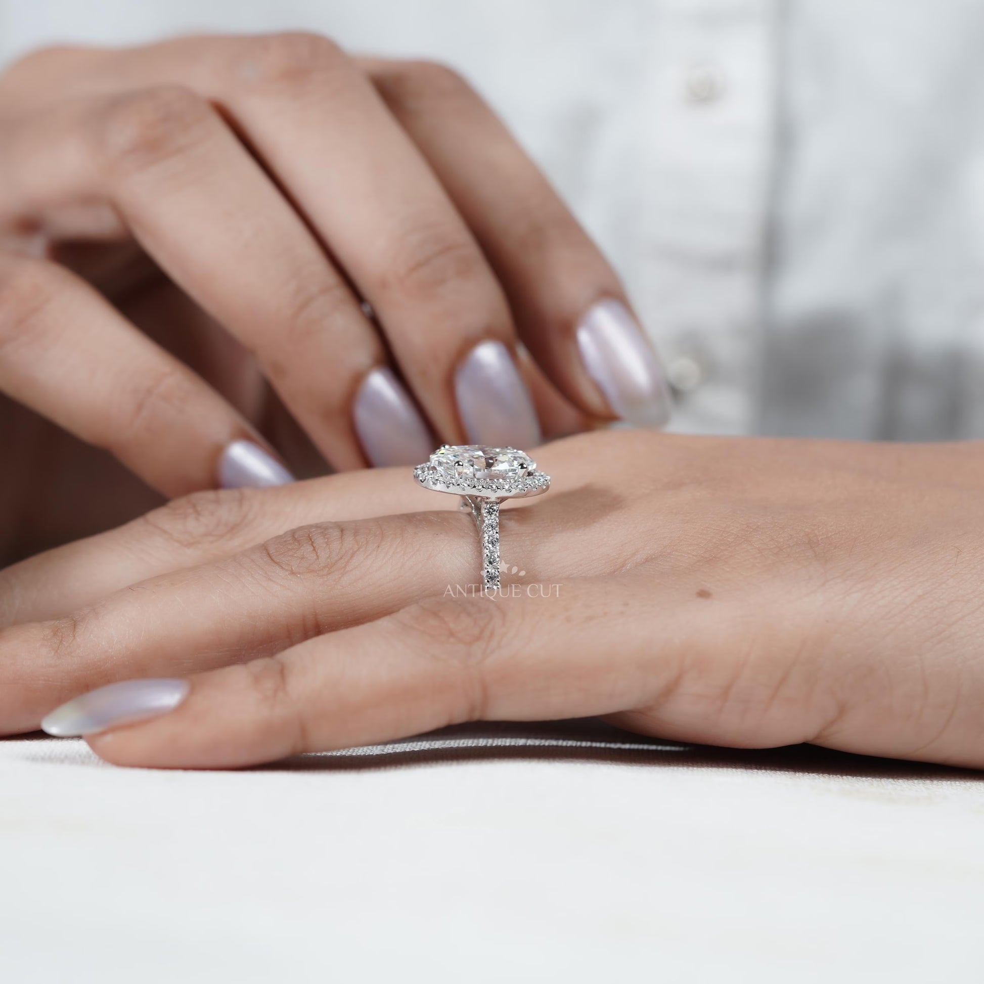 Diamond ring held by a hand with 'AntiqueCut' branding in the background
