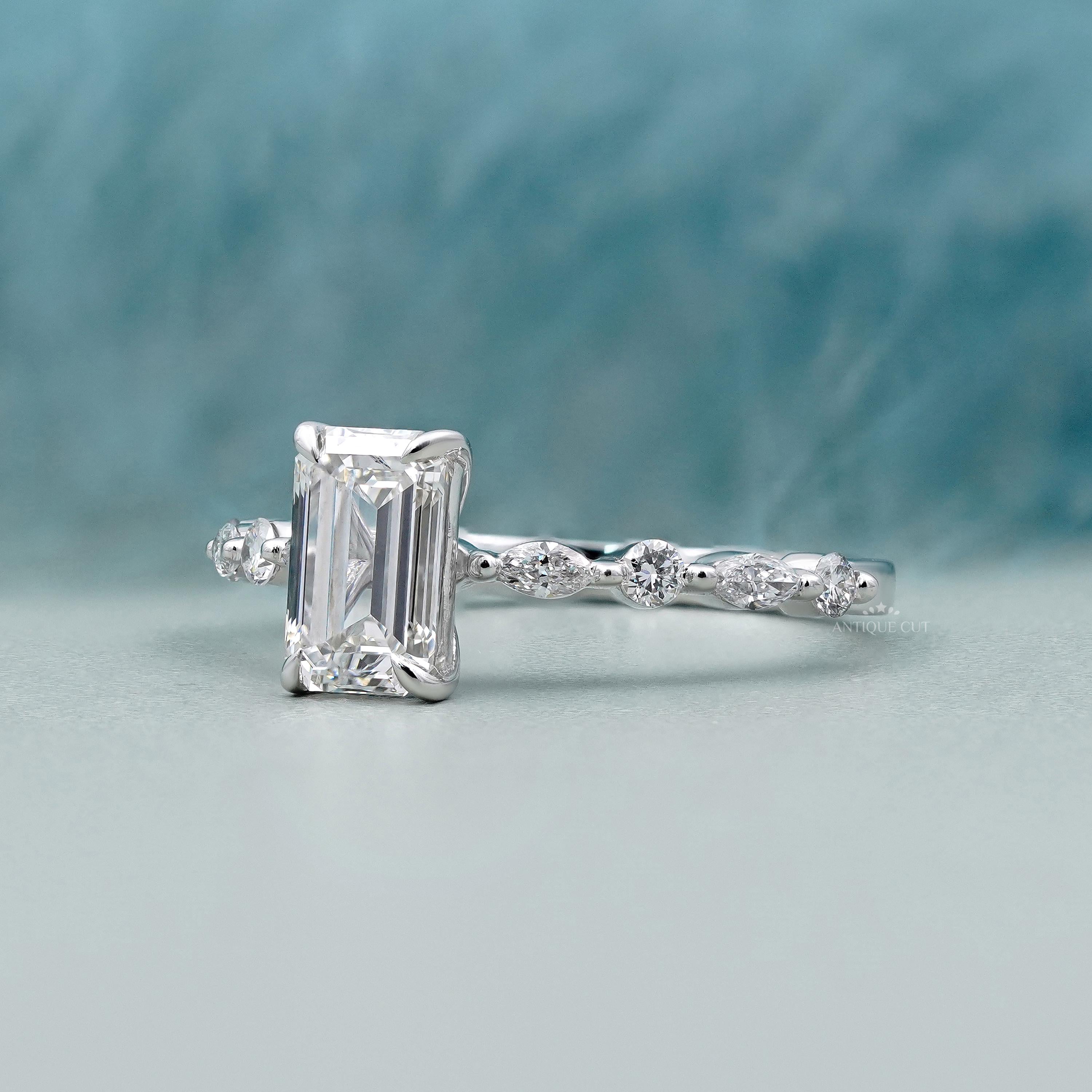 Silver ring with emerald-cut diamond and smaller diamonds on a light blue background

