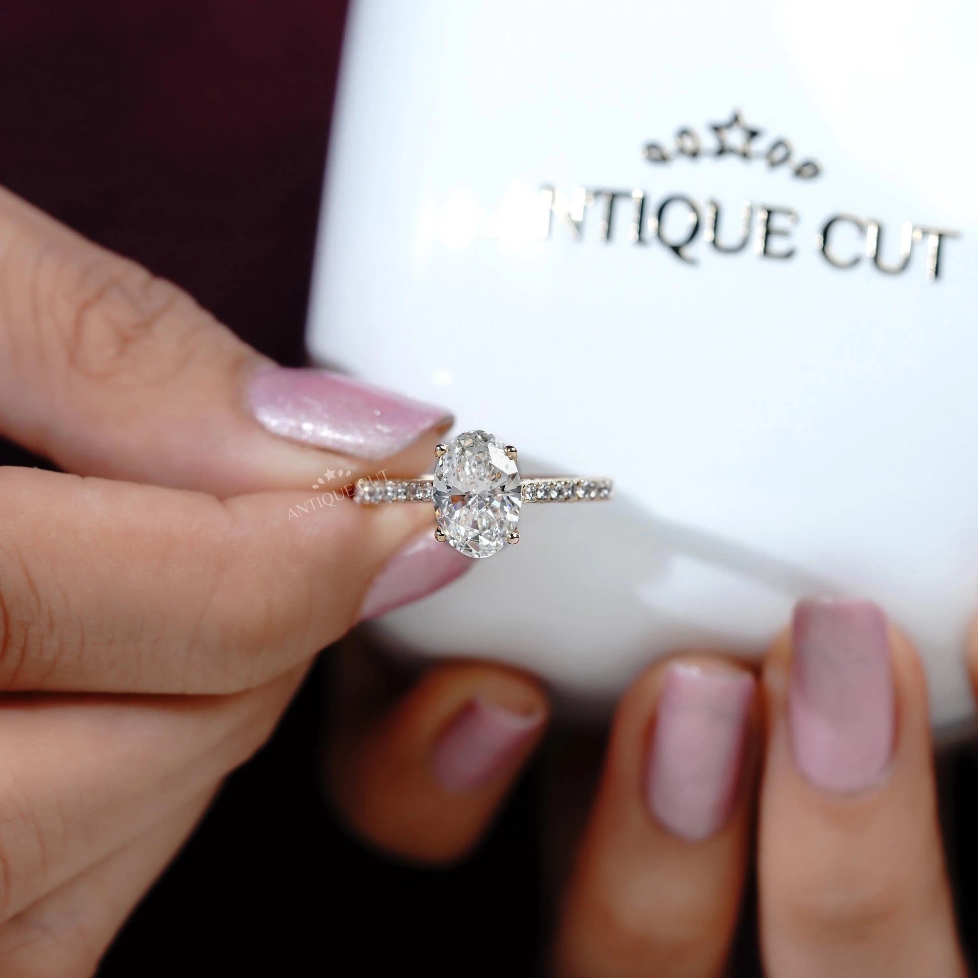 Hand holding a diamond ring with 'Antiquecut' branding in the background