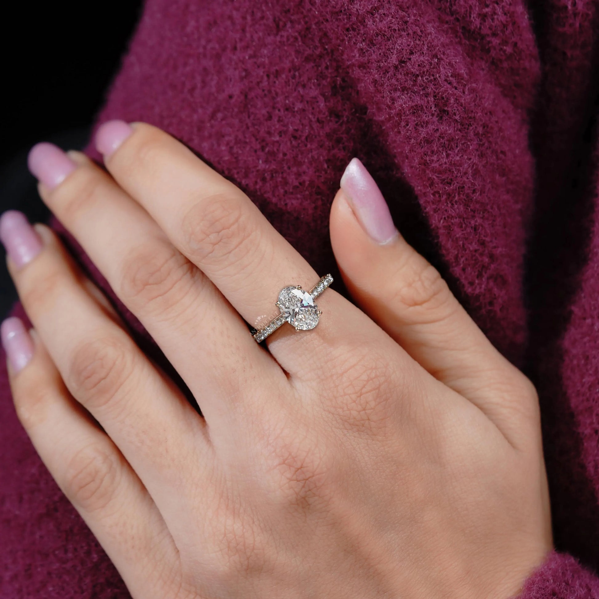 Close-up of a hand wearing a diamond ring with a blurred purple garment in the background