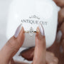Diamond ring held between fingers with 'AntiqueCut' branding in the background

