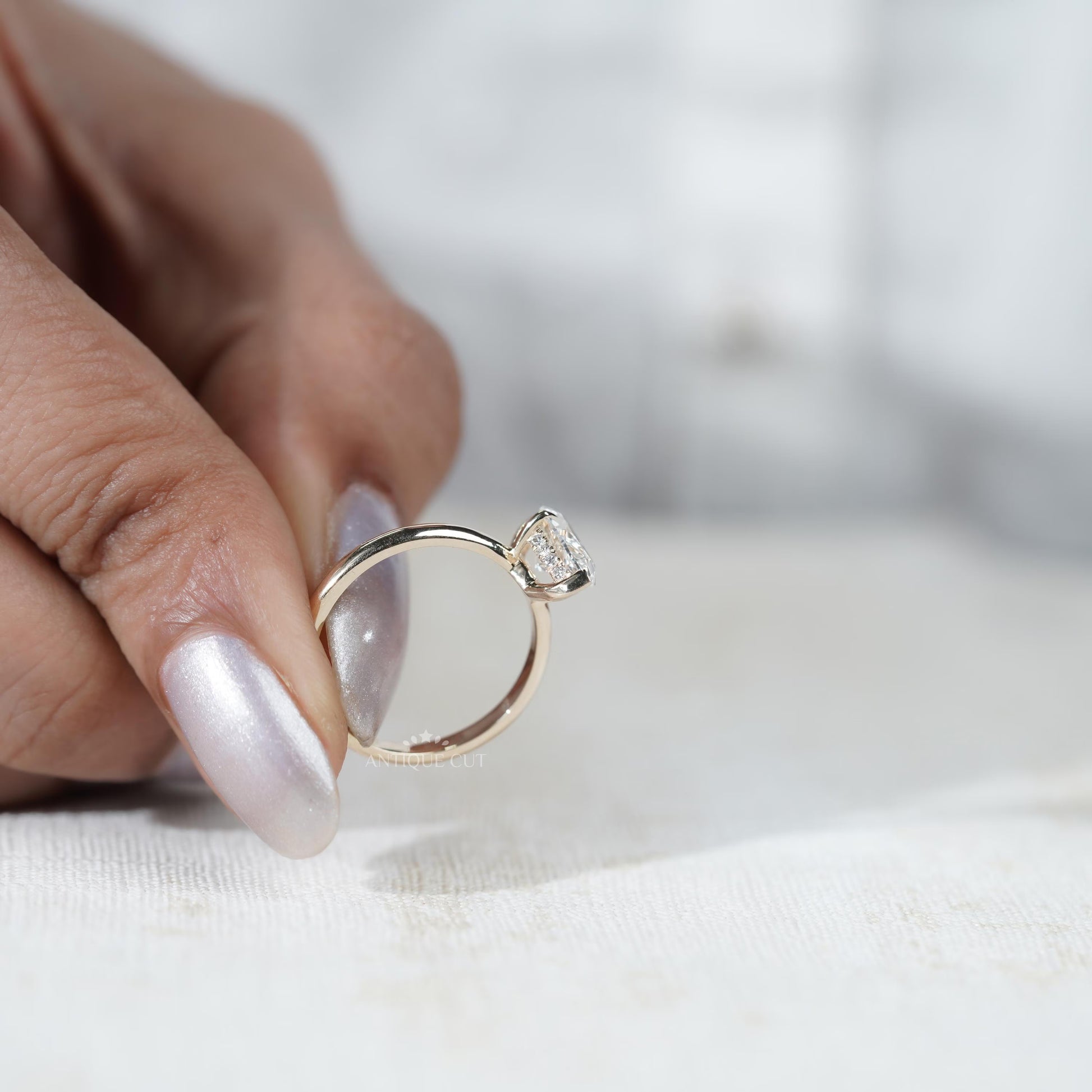 Diamond ring held between fingers with 'AntiqueCut' branding in the background
