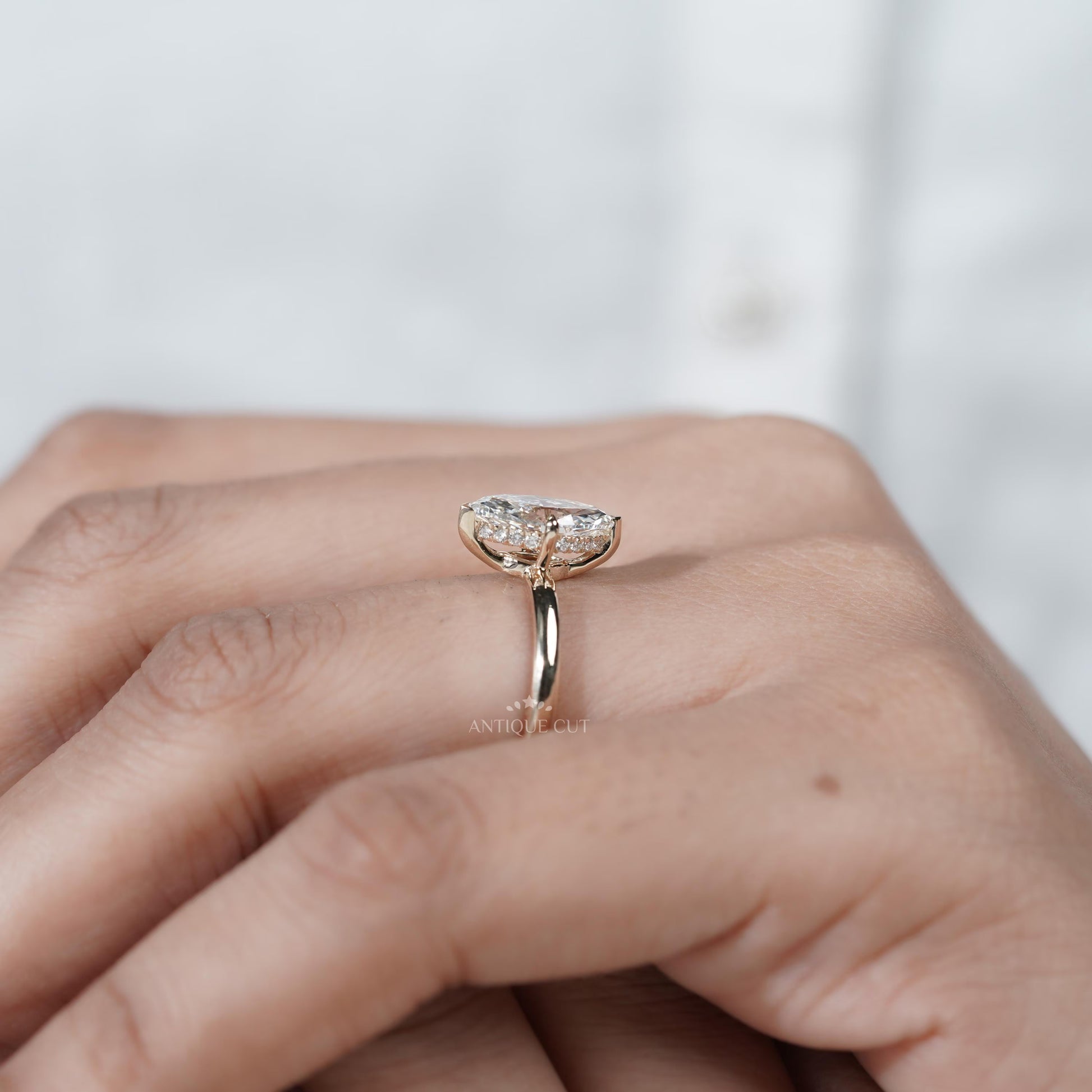 Diamond ring held between fingers with 'AntiqueCut' branding in the background
