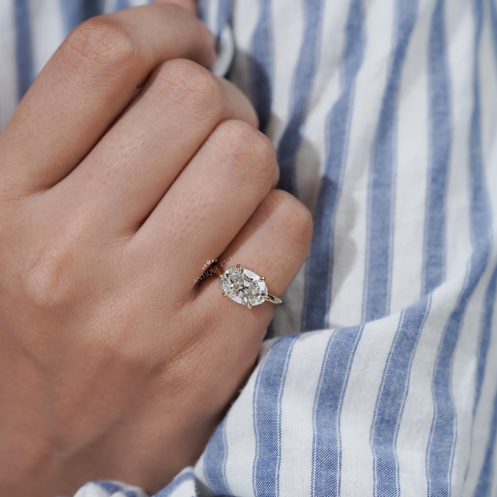 Hand wearing a diamond ring with a striped shirt background