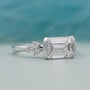 Diamond ring with emerald-cut center stone and smaller diamonds on a gradient background

