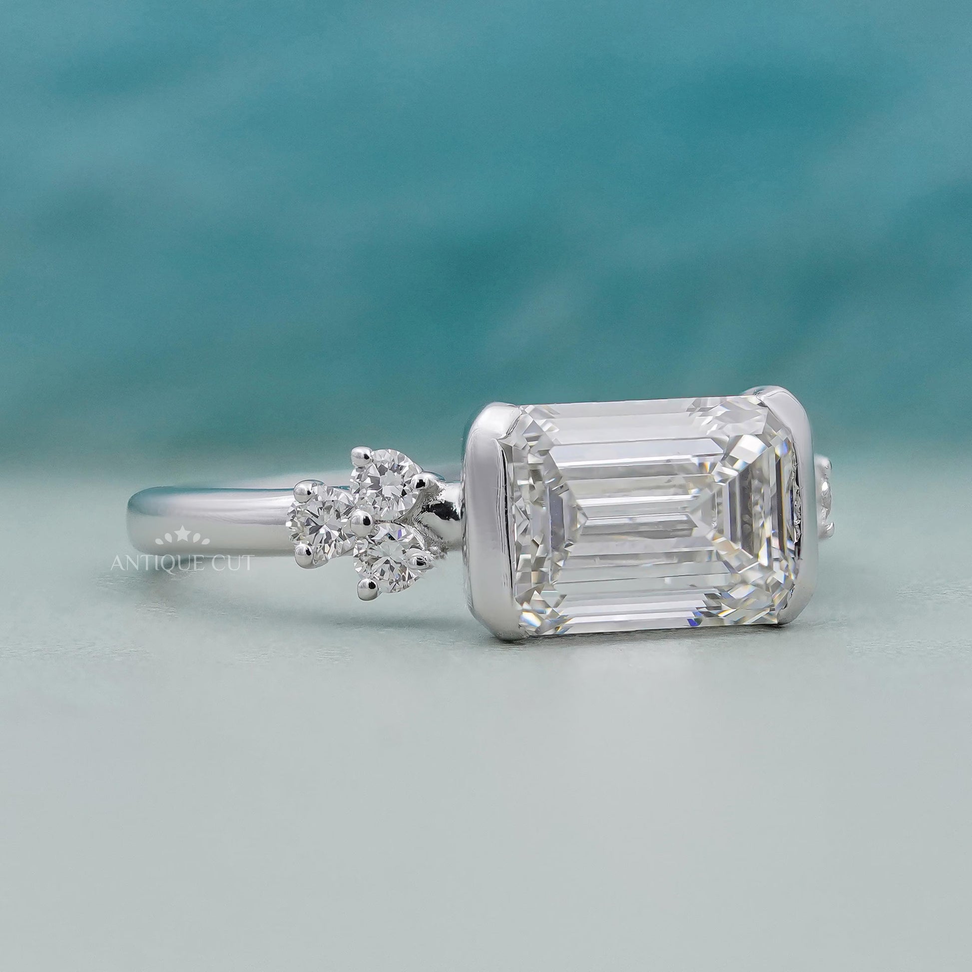 Diamond ring with emerald-cut center stone and smaller diamonds on a gradient background

