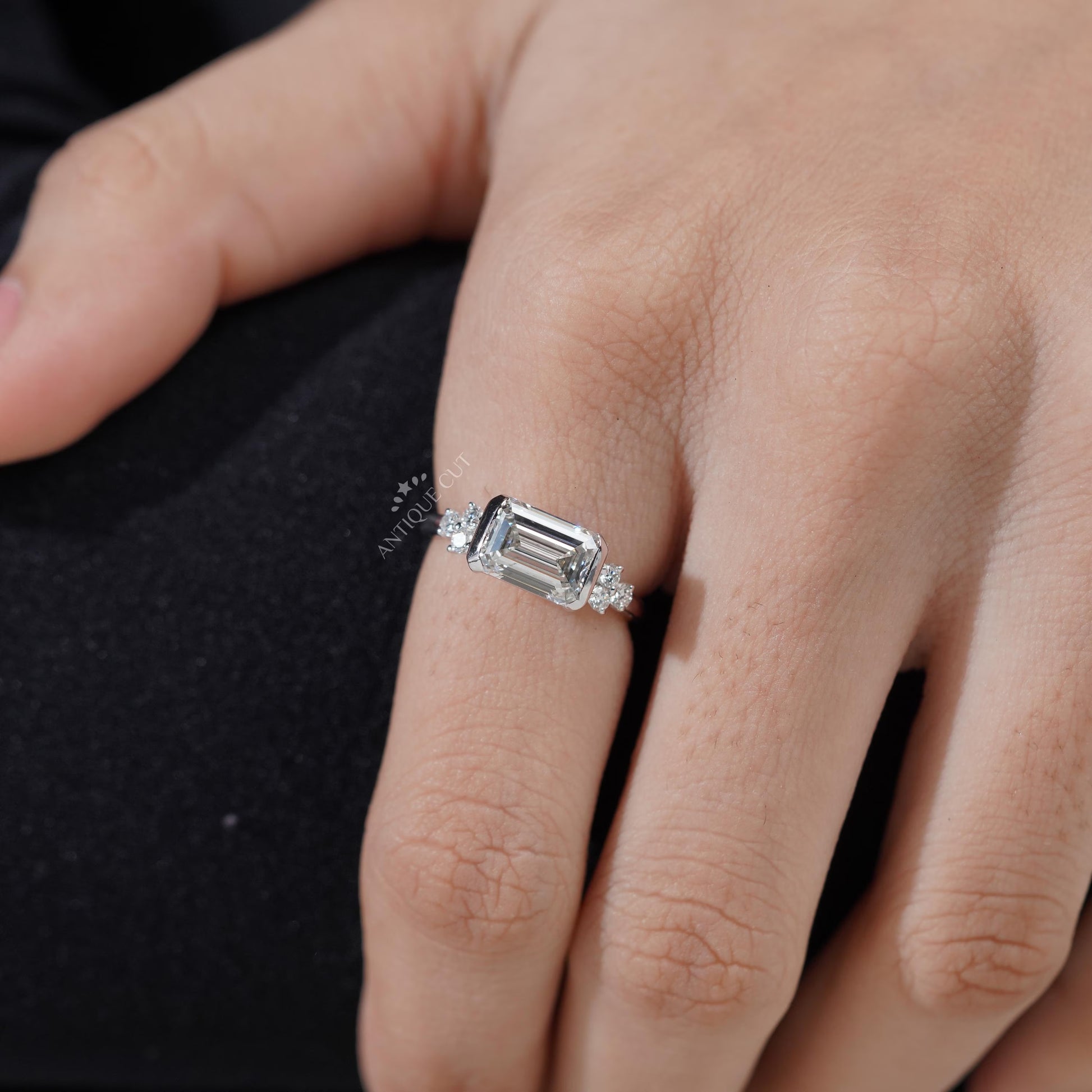 Diamond ring with emerald-cut center stone and smaller diamonds on a gradient background

