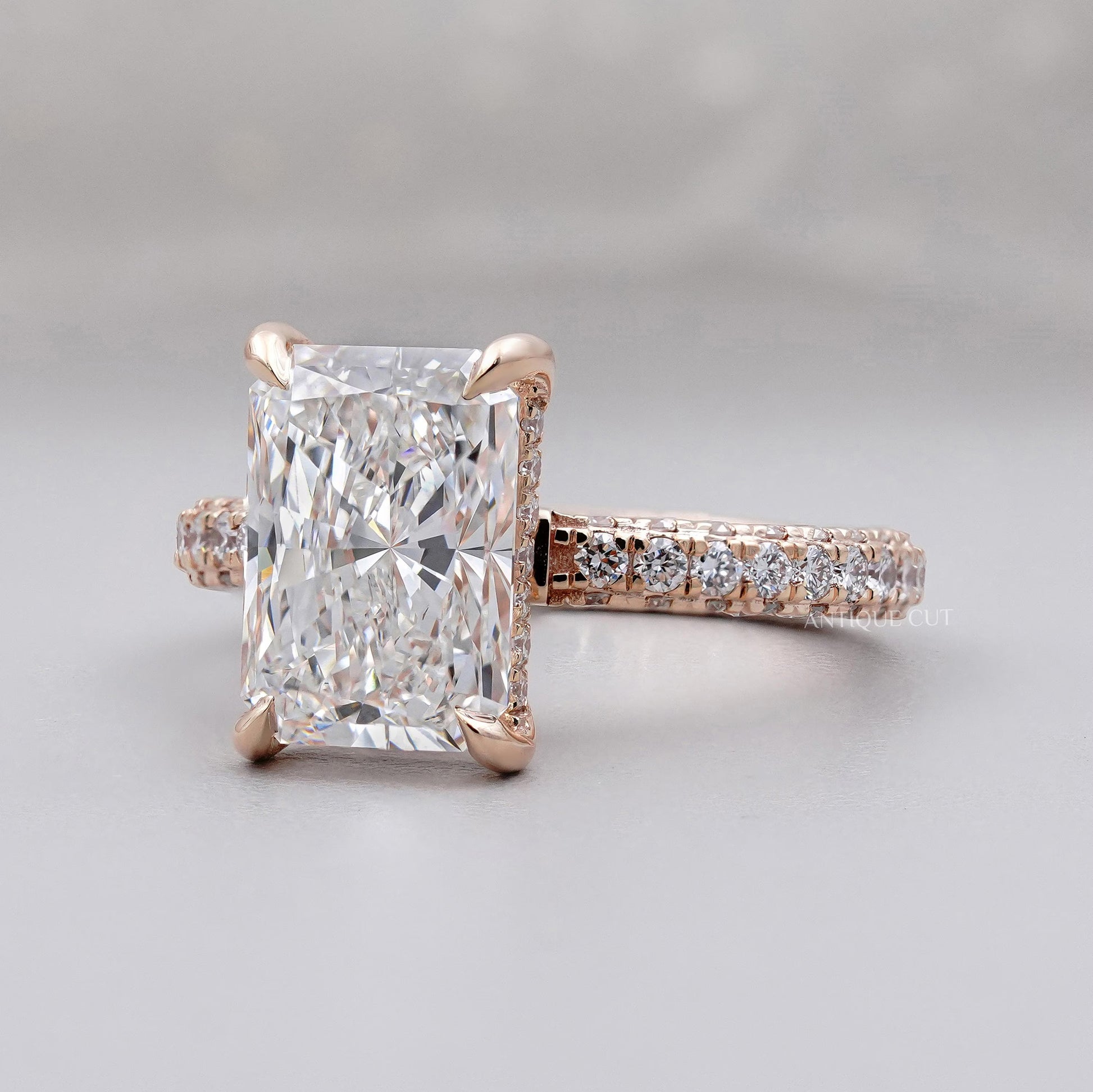Rose gold ring with a large diamond and smaller diamonds on the band against a gray background

