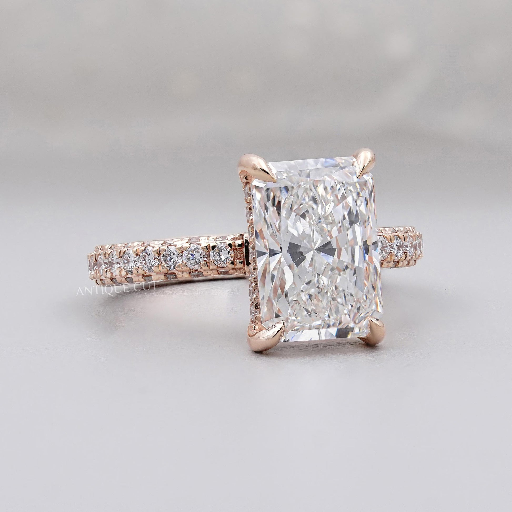 Rose gold ring with a large diamond and smaller diamonds on the band against a gray background

