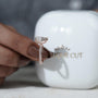 Diamond ring held by a hand with a blurred 'antiquecut' container in the background
