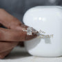 Diamond ring held by a hand with a blurred 'antiquecut' container in the background