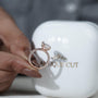 Diamond ring held by a hand with a blurred 'antiquecut' container in the background