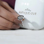 Diamond ring held by a hand with 'Antique Cut' branding in the background

