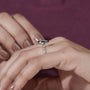 Close-up of a hand wearing a silver ring with a diamond on a purple background

