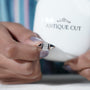 Close-up of a hand holding a diamond ring with 'Antiquecut' branding in the background.

