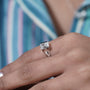 Close-up of a hand wearing a diamond ring with a colorful blurred background

