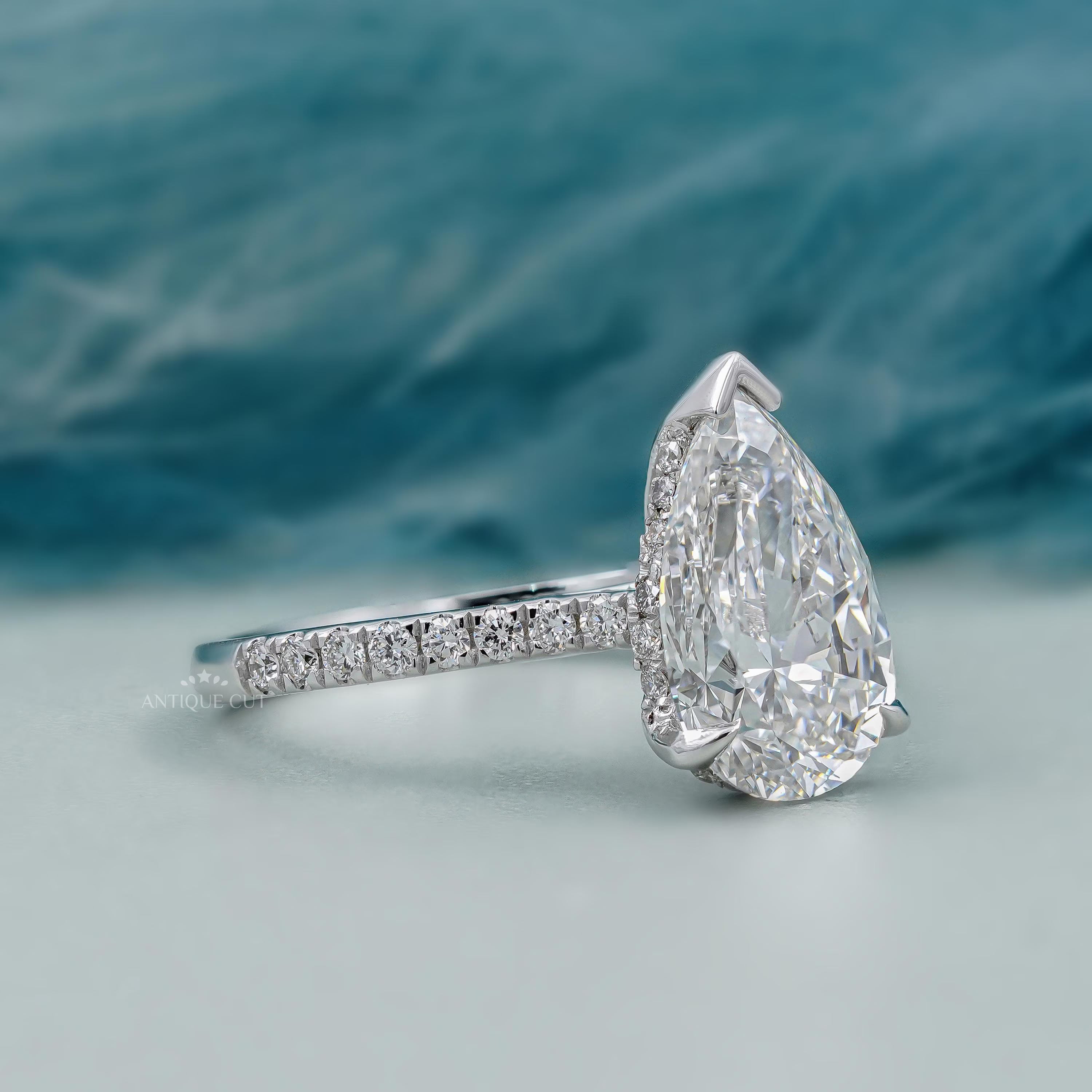 Diamond ring with a pear-shaped center stone on a soft blue background

