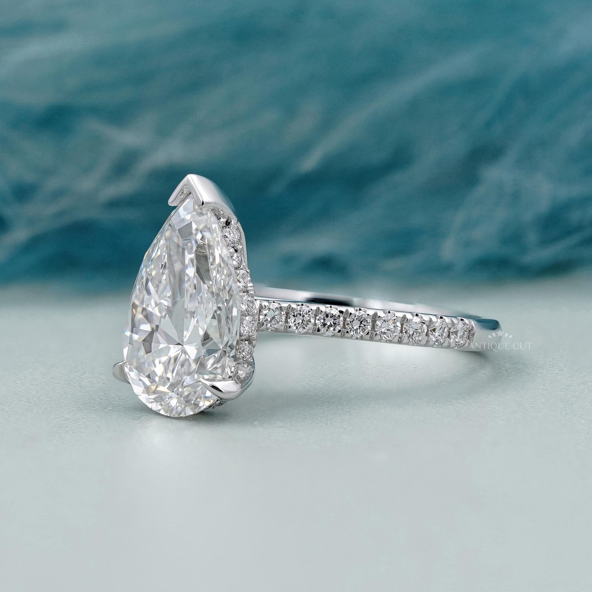 Diamond ring with a pear-shaped center stone on a soft blue background

