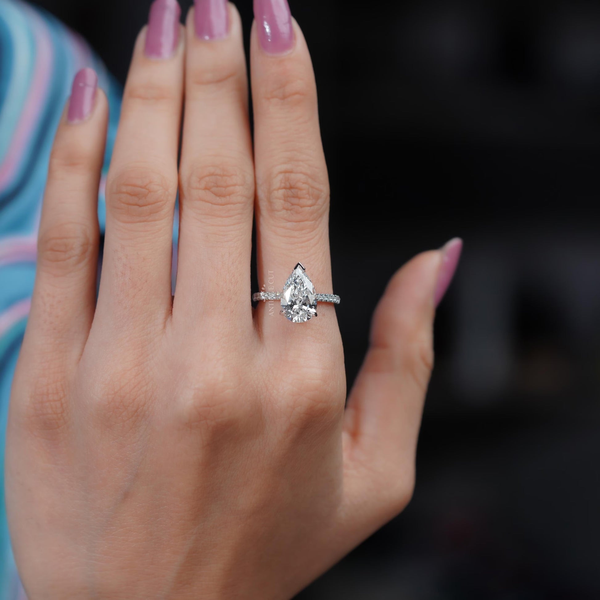 Diamond ring with a pear-shaped center stone on a soft blue background

