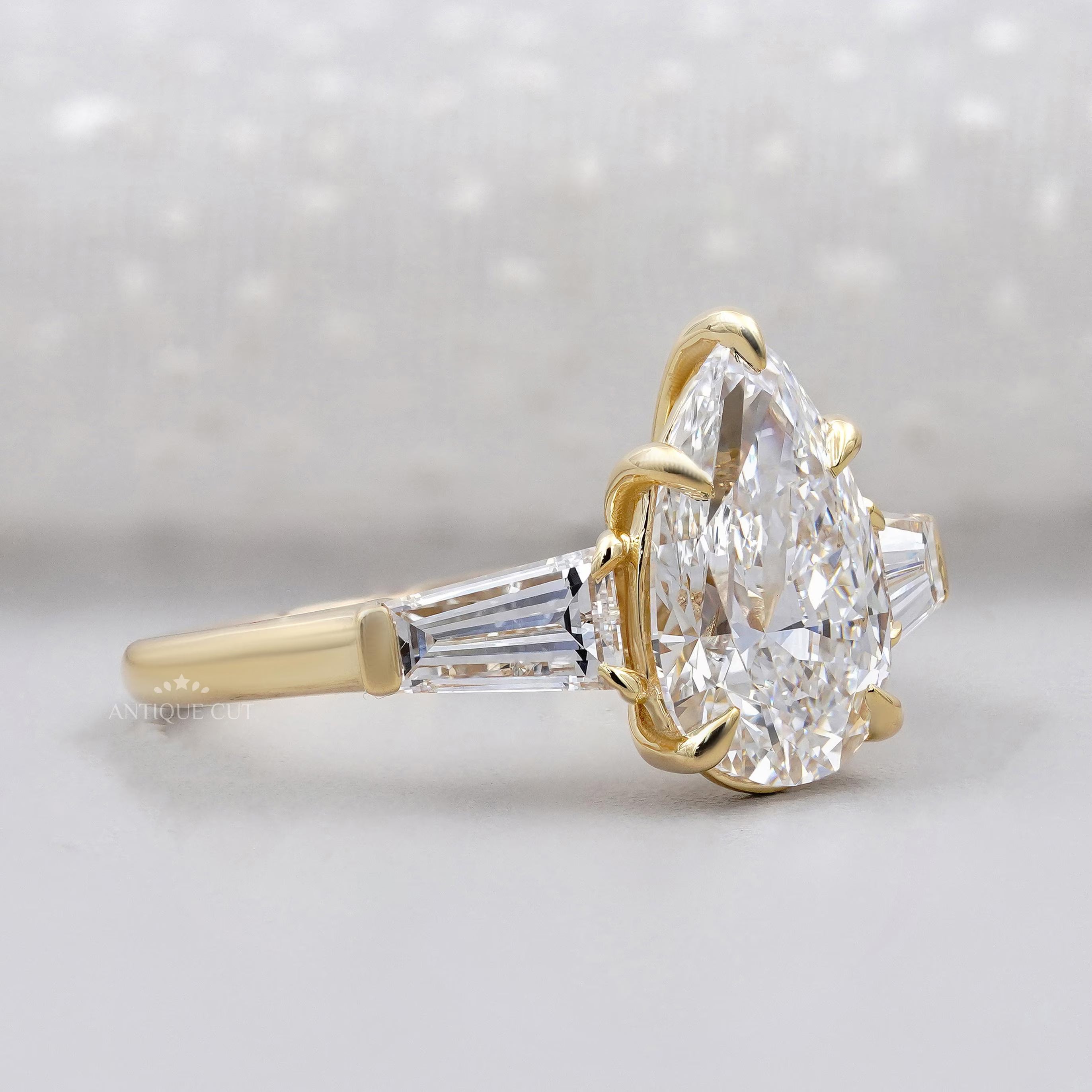 Gold ring with a large pear-shaped diamond and smaller baguette diamonds on a light gray background.