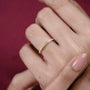 Gold ring with small diamonds on a finger against a red background

