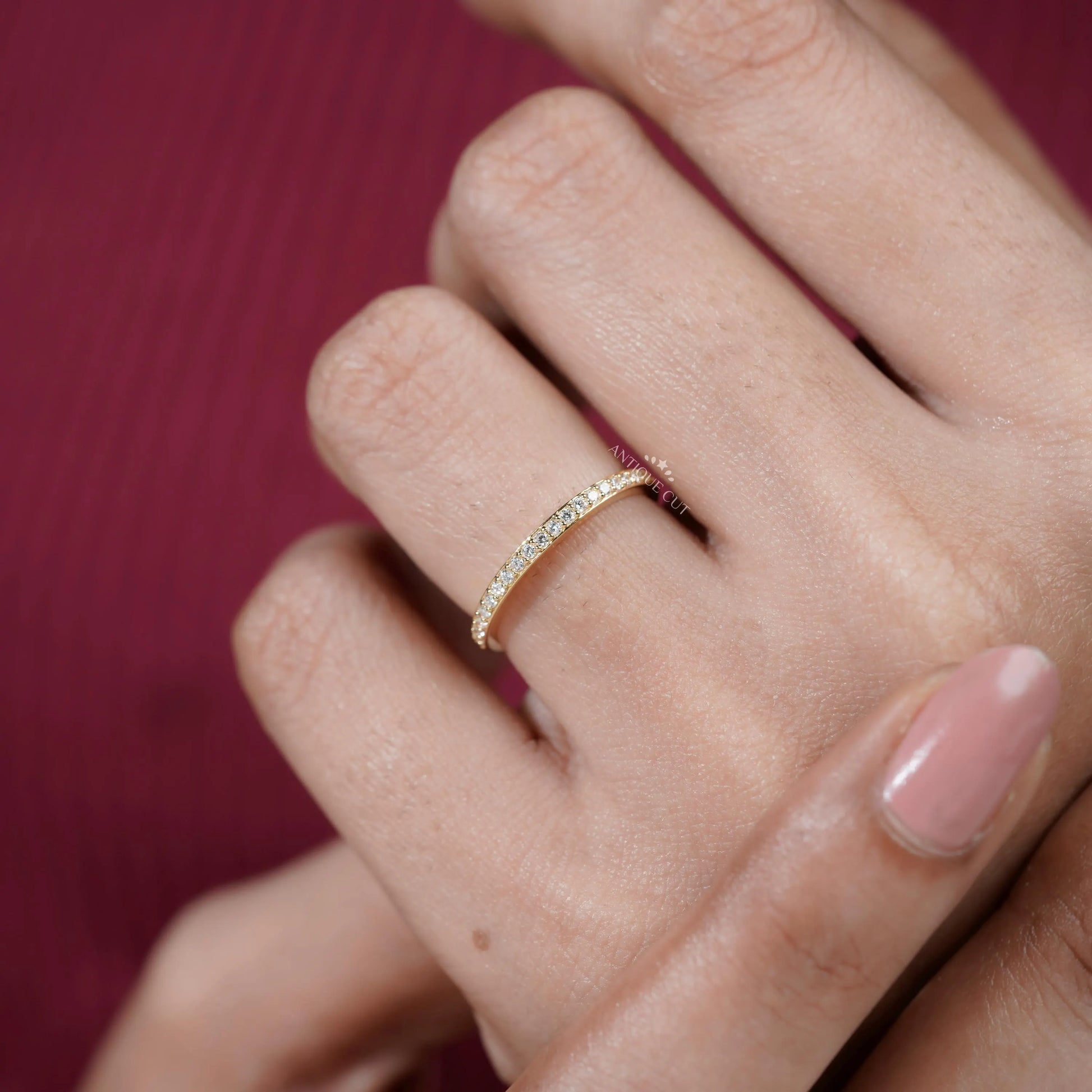 Gold ring with small diamonds on a finger against a red background

