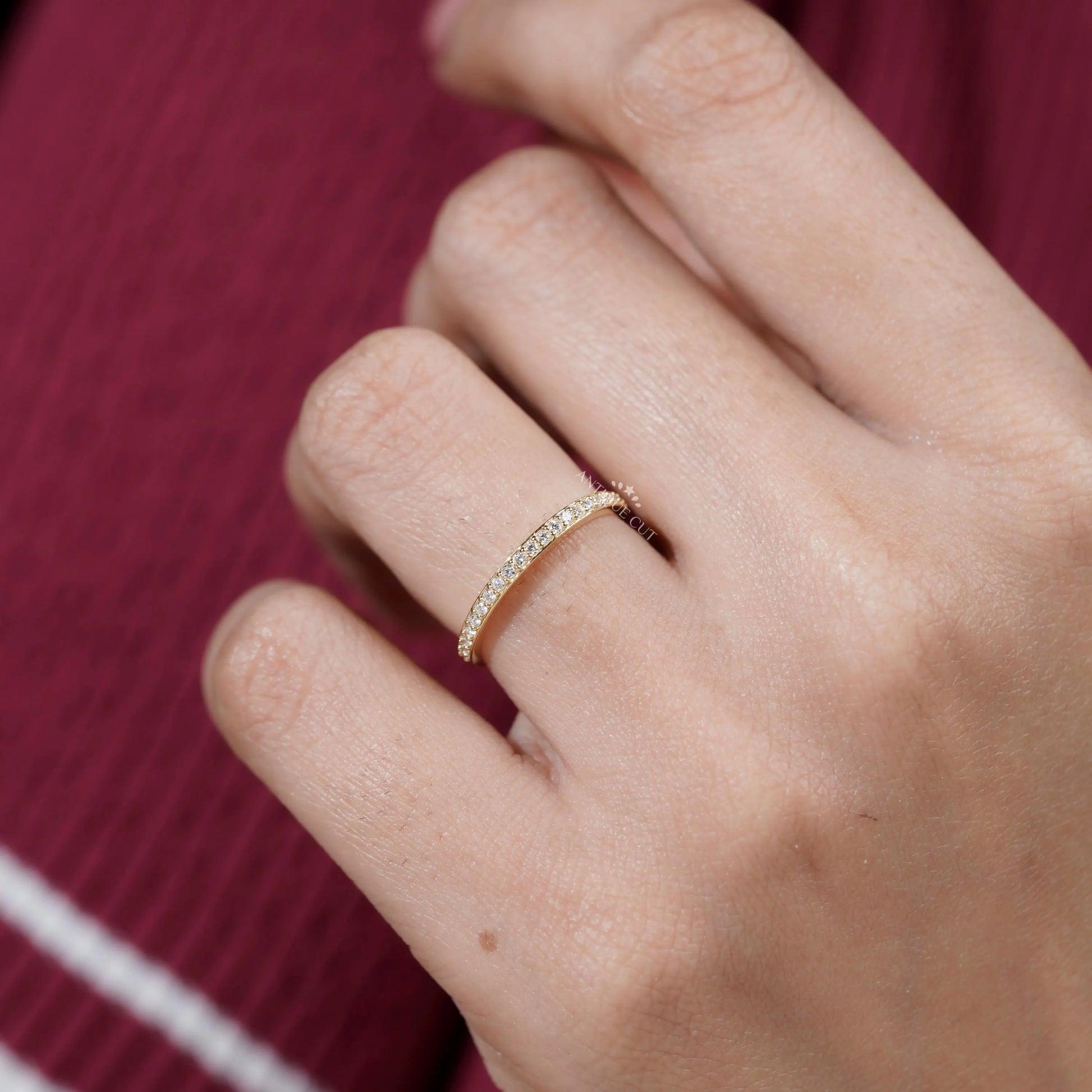 Gold ring with small diamonds on a finger against a red background

