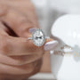Diamond ring held by a hand with 'AntiqueCut' branding in the background
