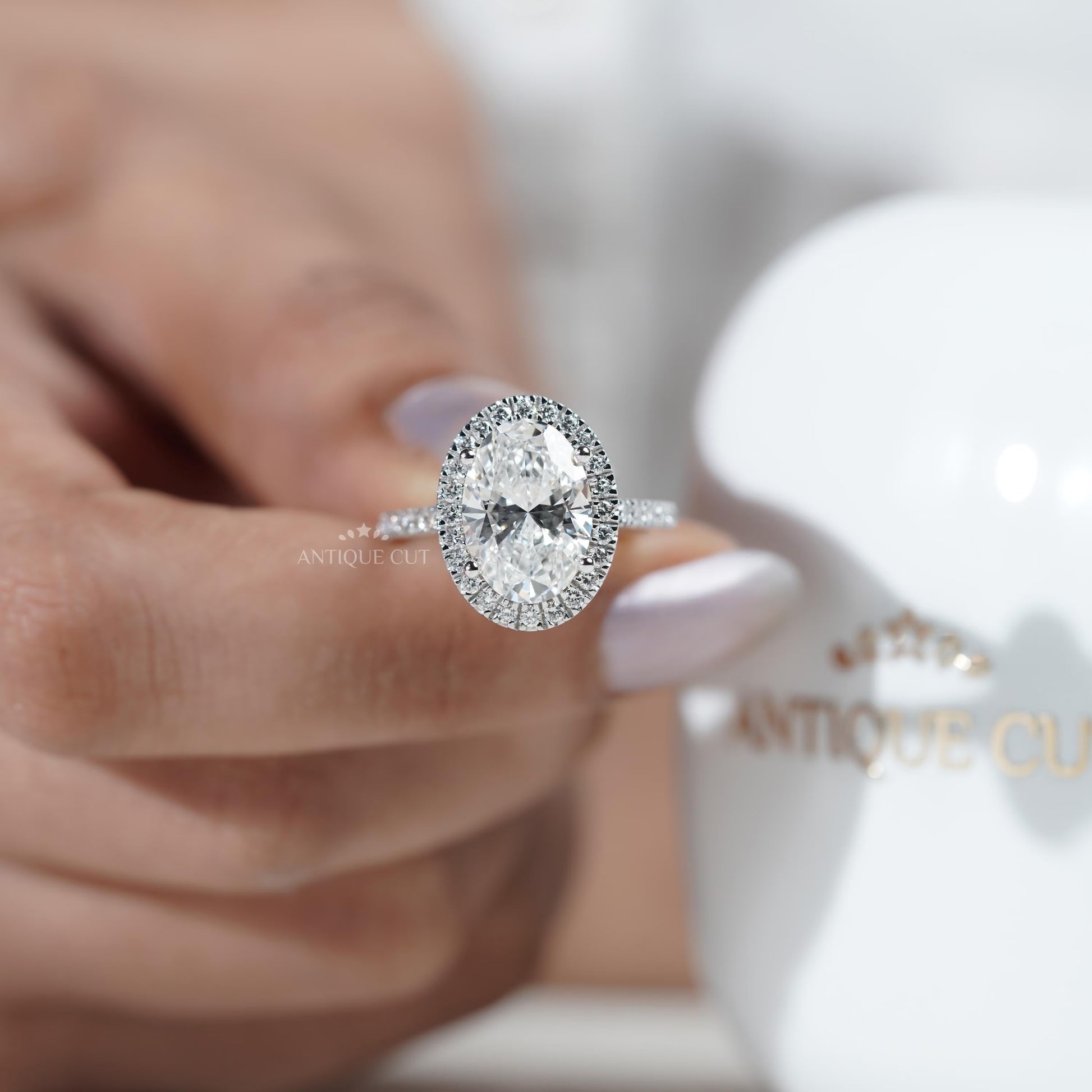 Diamond ring held by a hand with 'AntiqueCut' branding in the background
