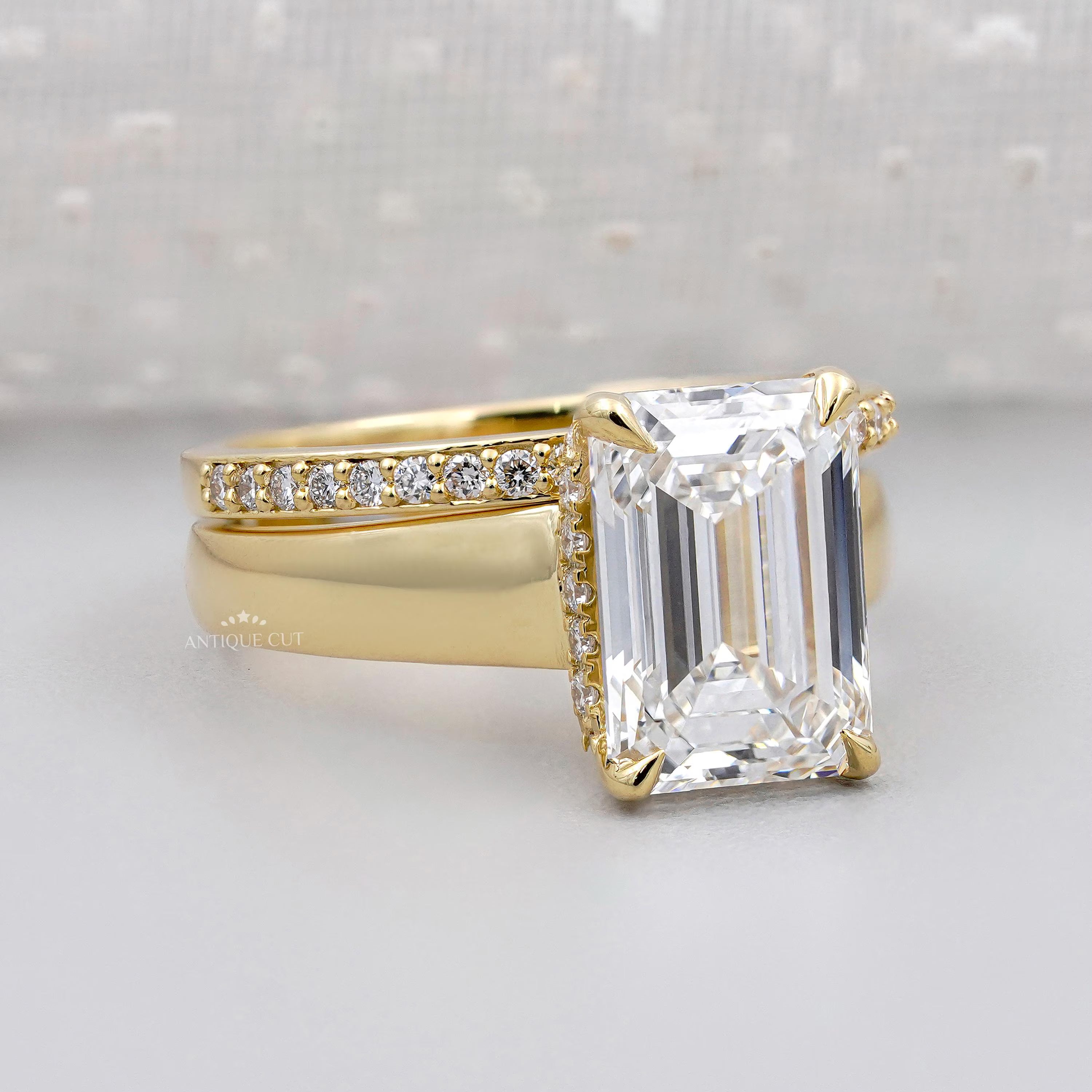 Gold ring with a large emerald-cut diamond and smaller diamonds on a light gray background