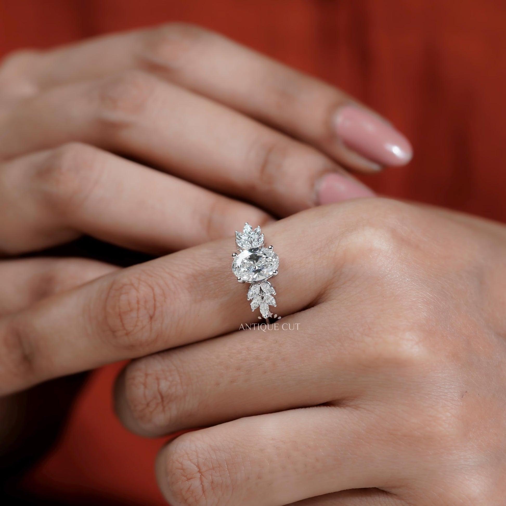 Close-up of a hand wearing a diamond ring with a blurred red background

