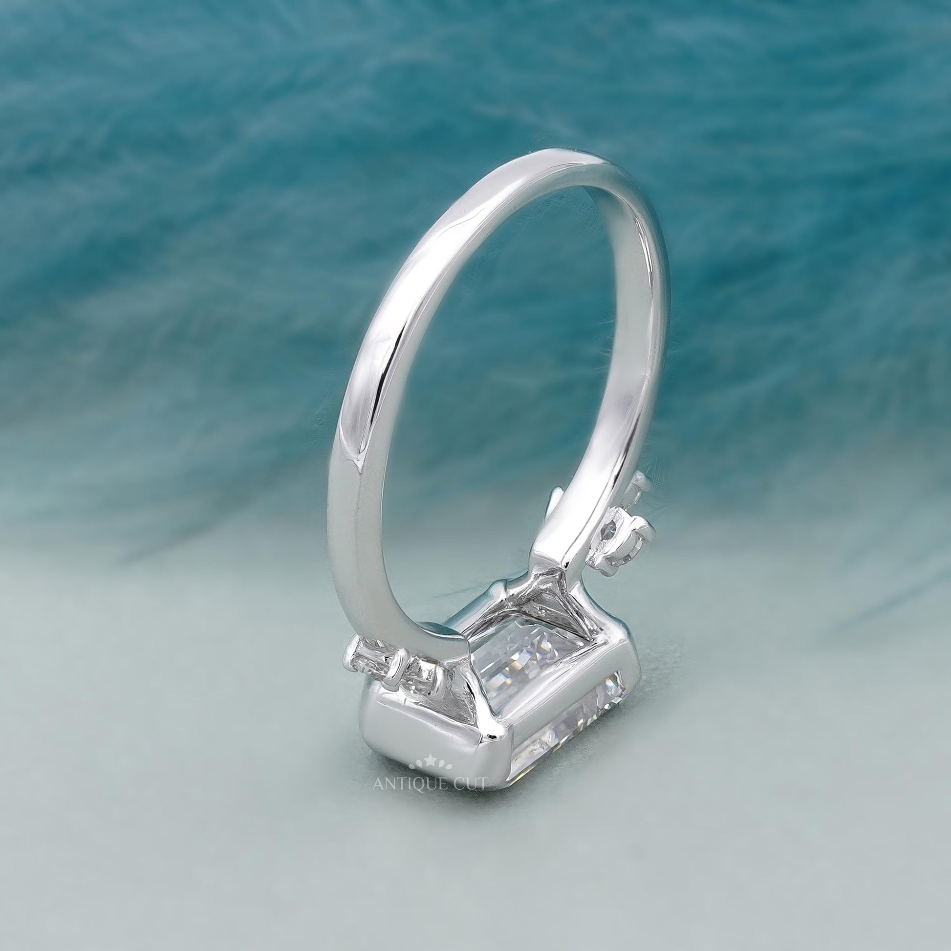 Diamond ring with emerald-cut center stone and smaller diamonds on a gradient background

