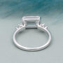 Diamond ring with emerald-cut center stone and smaller diamonds on a gradient background

