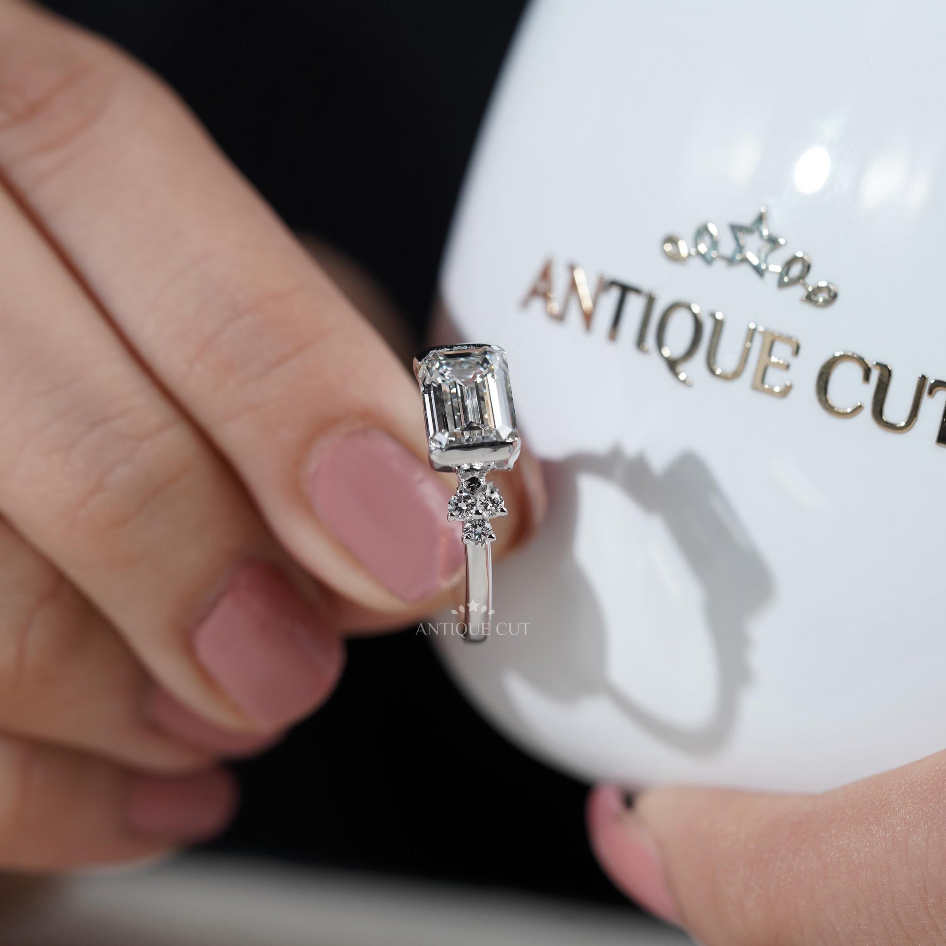 Diamond ring with emerald-cut center stone and smaller diamonds on a gradient background

