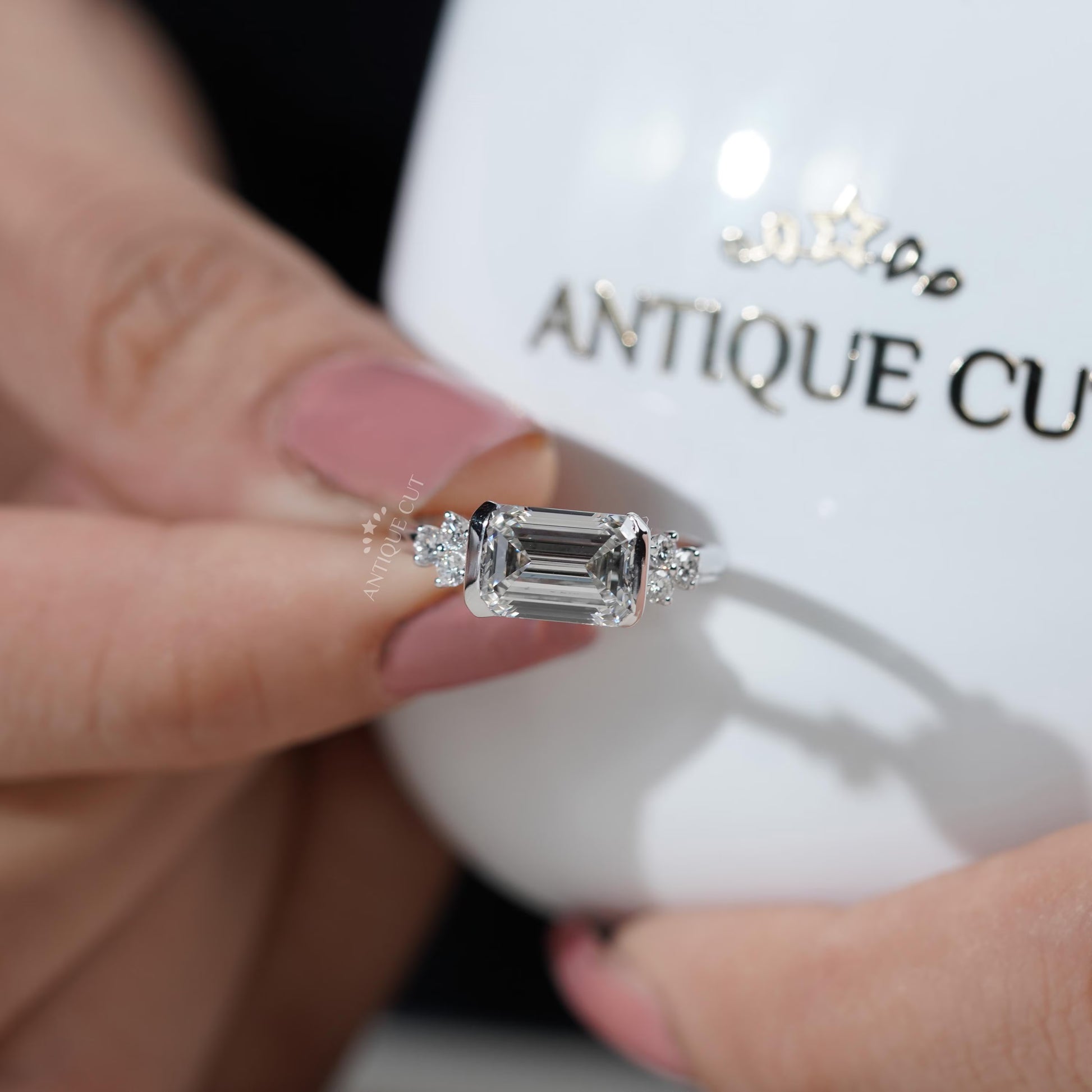 Diamond ring with emerald-cut center stone and smaller diamonds on a gradient background

